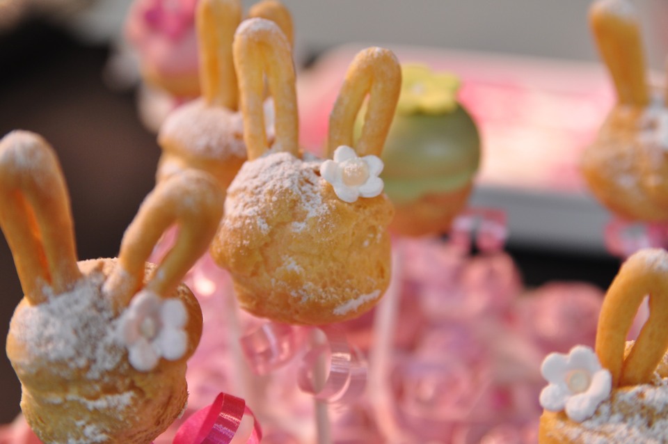 Cream puffs with bunny ears stand on a display decorated with pink flowers.